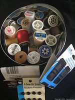 Tin filled with thread spools and unopened packs of needles and snaps