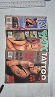 Front covers of three 1990s tattoo magazines laid out on table with ruler for scale