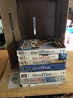 Stack of seven The Office DVD box sets inside cardboard divider