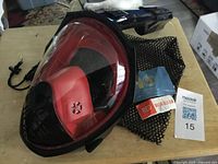 Front view of red/black full-face snorkel mask on mesh bag with tags visible