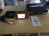 Camera powered on with charger, AV cable, box and MaxSold card visible