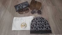 Group shot displaying all items: beanie, dust bag, two sunglasses, Guess pouch, brown hard case