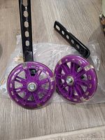 Two purple training wheels with attached black brackets on packaging