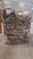Full view of plastic container showing mixed jewelry contents including cuff bracelet, chains and beads
