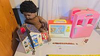 Overview showing doll, wooden lock house, Fisher-Price TV and pink dollhouse piece
