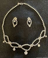 Full view of rhinestone necklace and matching screw-back earrings on black background