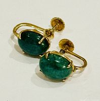 Pair of yellow gold earrings with oval green cabochon gemstones showing the front view and screw back closures.