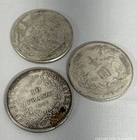 Three collectible coins shown together, including one French 10 Francs coin dated 1967 and two Chinese coins with detailed designs.