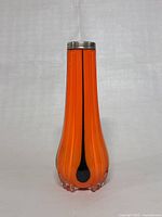 Front view of tall coral orange art glass vase with black teardrop accents and silver rim on top.