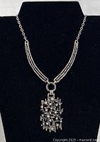 Silver-tone brutalist/modernist necklace on black bust showing pendant and chain details.