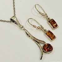 Necklace chain and pendant with round amber shown alongside pair of rectangular amber earrings on white background.
