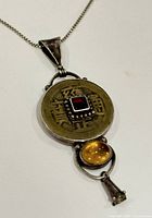 Close detail of the pendant showing Asian coin design with garnet and topaz stones, mounted on silver pendant and chain.