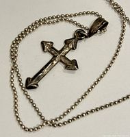 Close-up of silver cross pendant with arrowhead tips on ball chain necklace.