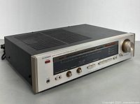 Front and angled side view of Luxman R-404 stereo receiver showing silver front panel with tuning window, knobs, and buttons, placed on flat surface.