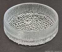 Clear glass bowl showing bubble-like textured bottom and frosted vertical striped sides on black surface background.