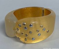 Front view of translucent yellow Lucite bangle with silver and gold-tone studs on textured surface.