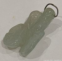 Top-side view of light green translucent hand carved jade pendant with metal loop for hanging