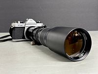 Side angled view of Pentax K1000 with Unitax telephoto lens attached, showing lens length and camera body detail.