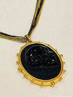 Close-up of the oval pendant showing the black skull design with gold-tone frame and ball details.