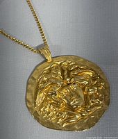 Front close-up view of the gold-tone Medusa pendant showing detailed textured features and chain attachment.