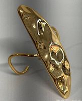 Close-up side angle of the gold-tone modernist style bangle showing textured, hammered surface and curved open cuff design.