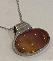 Close-up photo of the oval amber stone pendant set in silver with attached chain.