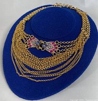 Multi strand gold-tone chain necklace on blue display pad showing overall design and clasp detail with colored rhinestones.
