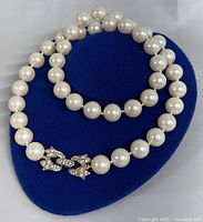 Necklace laid on blue jewelry display showing pearl beads and rhinestone clasp.