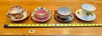 Photo showing the four teacup and saucer sets lined up with scale for size reference.