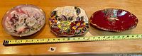 Three assorted decorative plates on wood surface with tape measure displayed for scale