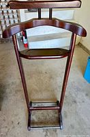 Full view of the wooden valet stand showing the hanger, accessory tray, and trouser bar.