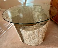 Full view of the coffee table showing the round glass top resting on the abstract textured stone base with spherical accent.