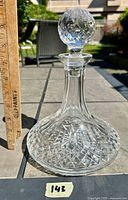 Full view of the cut glass decanter with a ruler showing approximate height, clear base with diamond cut patterns and starburst design.