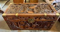 Top and front view of the carved camphor wood chest showcasing intricate Chinese traditional scenes and brass corner accents.