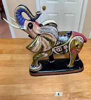 Side view of the hand-painted elephant figurine with raised trunk showing colorful detailed design and black base with red/gold lining