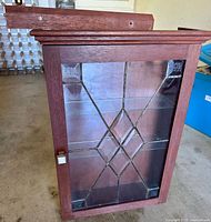 Front view of the handcrafted wooden wall-mounted display cabinet showing the leaded clear glass door with geometric diamond pattern and wooden frame.