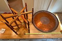 Photo showing the wooden folding base standing next to the copper tray, illustrating table components and size scale with visible measuring tape.