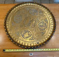Photo of top side of large round brass tray showing detailed engraving, central courtly figures, smaller surrounding vignettes, and scalloped rim with silver inlay accents.