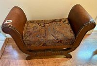Front view of brown leather frame footstool/bench with brass nailhead trim and paisley fabric cushion top on wood base