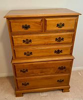 Front view of light wood chest of drawers showing five drawers with metal decorative handles.