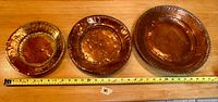 Front view of three hand-hammered copper wall plates arranged in descending size order on a wooden surface showing warm reddish patina and scalloped rims.