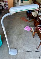 Full view of white Ott-Lite floor lamp showing flexible gooseneck arm, rectangular lamp head, and base on concrete floor.