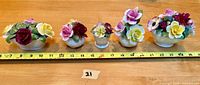 Five hand-painted floral porcelain arrangements laid out next to a tape measure for size reference, measuring approximately 23 inches total width.