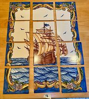 Top-down photo showing all 12 hand-painted ceramic tiles arranged in a 3x4 grid to display the full mural of a tall sailing ship at sea with decorative floral and scroll border.