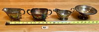 Four silver serving pieces laid out with measuring tape showing sizes in inches: two gravy boats and two handled sugar bowls/scuttles.