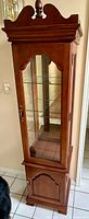Front view of entire wooden curio cabinet showing glass-fronted upper door and solid wood lower door.
