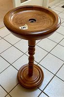 Full view of the turned wood pedestal stand showing the circular dished top, turned column, and base on tiled floor.