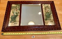 Full front view of the three-panel mirror showing oak frame and two chromolithograph side panels flanking the central beveled mirror, with measuring tape showing width.