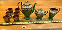 Full set shown with ruler for scale: coffee/tea pot, sugar bowl, creamer, and six cups, all with green glaze, gold moriage, and white floral hand-painting.