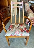 Front view of vintage wooden armchair showing floral upholstered seat, wooden armrests, and vertical slat backrest.